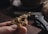 A hand holding a detailed, golden dragon-shaped pendant. The texture and intricate design of the dragon are highlighted against a softly blurred background, which includes a closed pocket knife nearby.