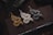 Three intricately designed dragon figurines in gold, silver, and bronze are arranged on a dark book or notebook. Below the figurines, a black tactical pen is placed horizontally. The setting is dimly lit, adding a sense of mystery and elegance.