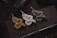 Three intricately designed dragon figurines in gold, silver, and bronze are arranged on a dark book or notebook. Below the figurines, a black tactical pen is placed horizontally. The setting is dimly lit, adding a sense of mystery and elegance.