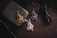 Three intricate dragon-shaped pendants in gold, silver, and bronze are arranged on a wooden surface. Nearby items include a metallic flask, a folding knife, and a pen, creating a rustic and rugged atmosphere.