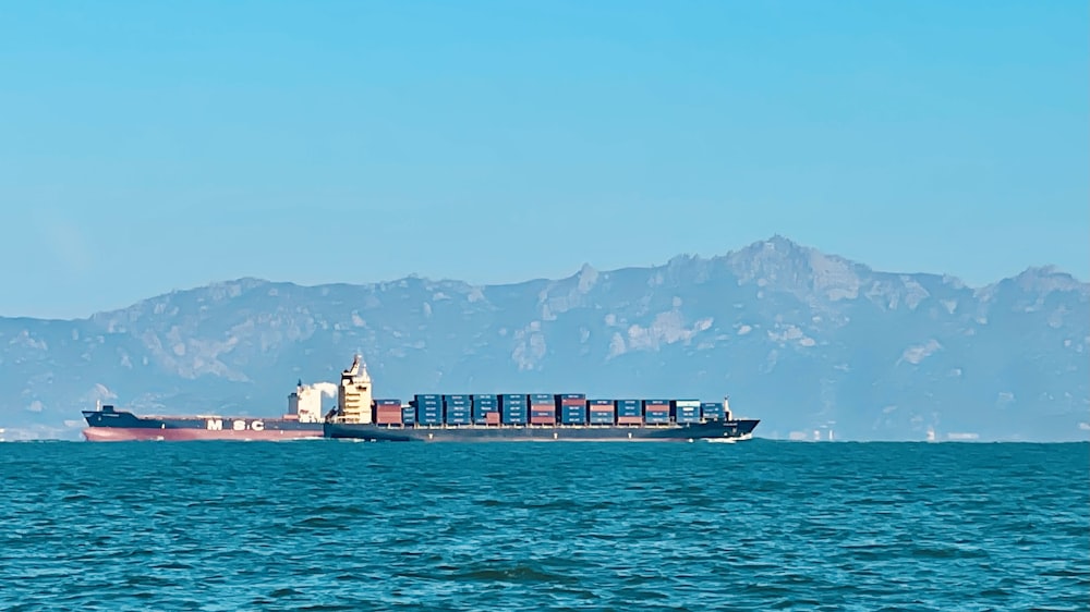 a large cargo ship in the ocean with mountains in the background