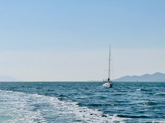 A sturdy sailboat cutting through open ocean waves under a bright sky.