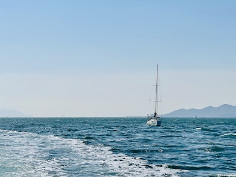 A sturdy sailboat cutting through open ocean waves under a bright sky.