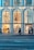 A modern storefront for the brand Fendi features large glass windows with illuminated displays. People walk along the sidewalk in front of the store, showcasing a bustling urban environment. The store's design includes tall, arched sections that are visually striking.