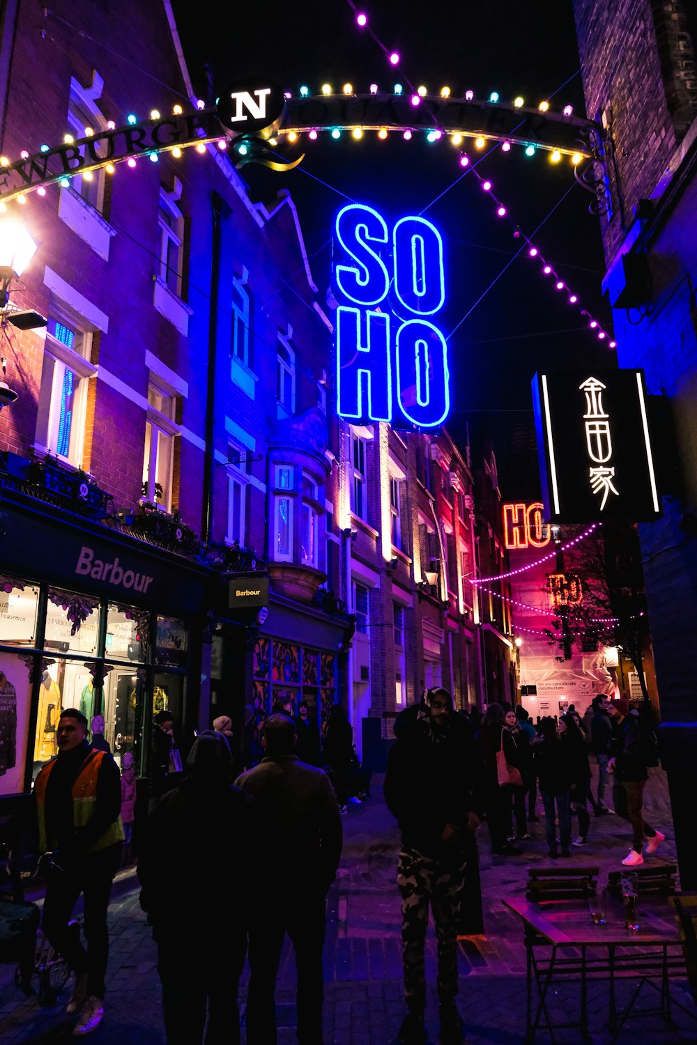 a group of people walking down a street under a neon sign