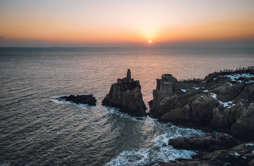 the sun is setting over the ocean near a rocky shore