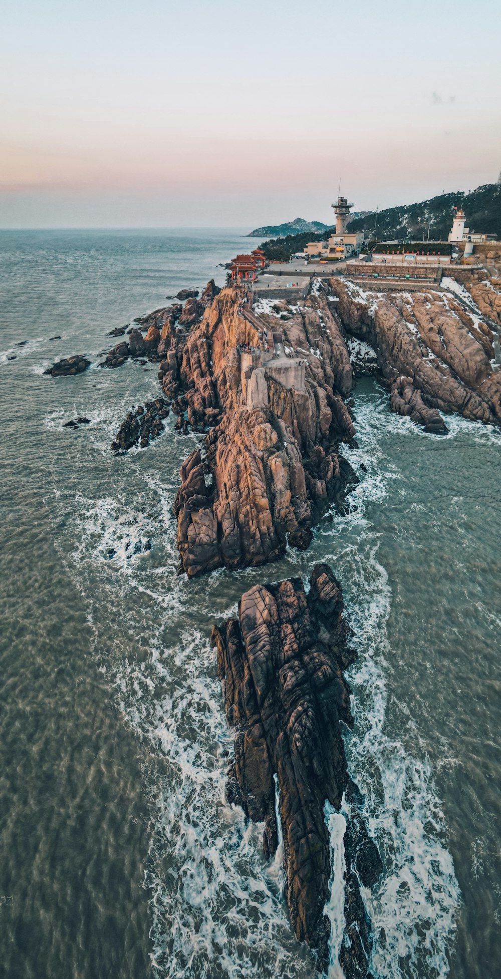 an aerial view of a rocky coastline with a lighthouse in the distance