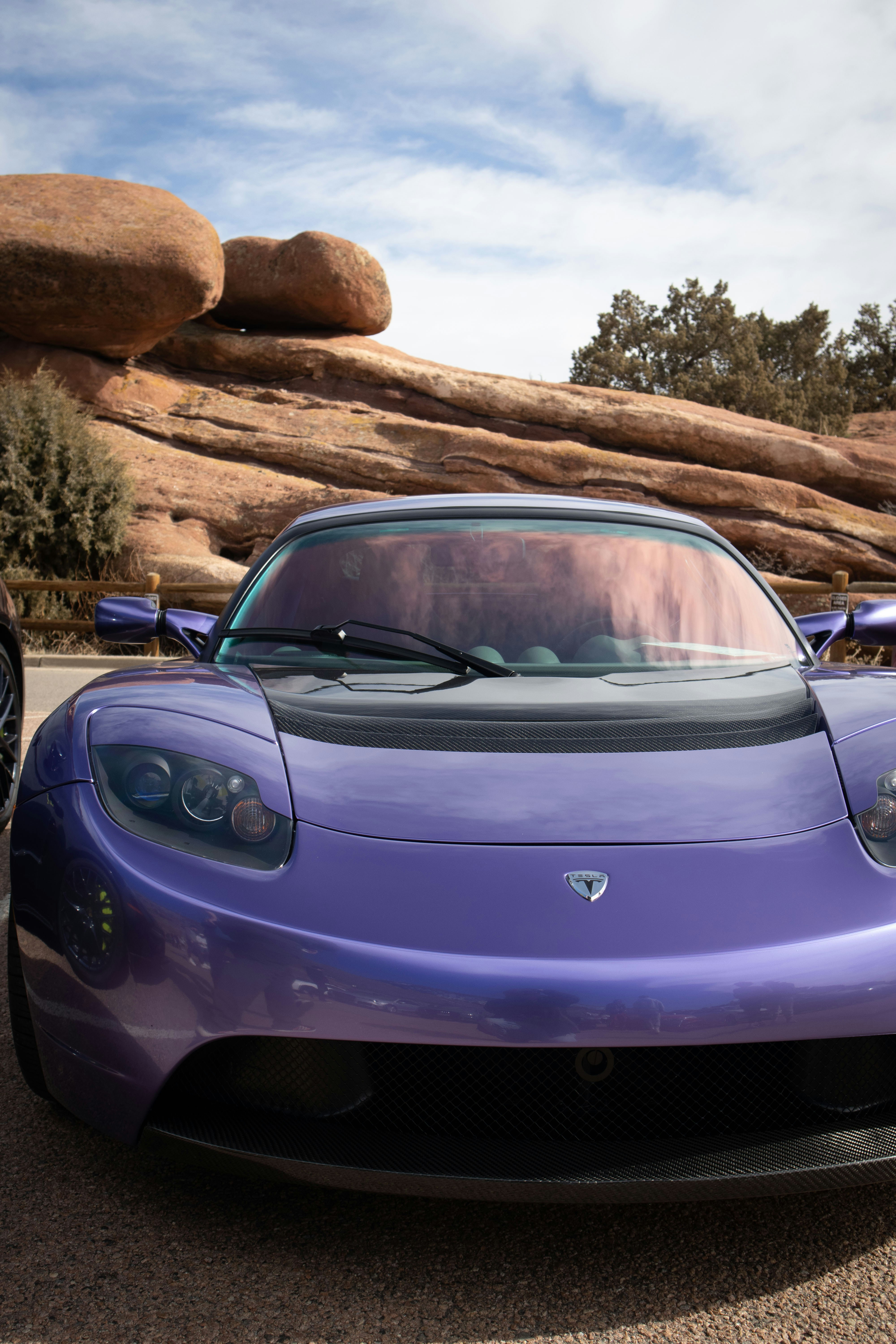 Ein lilafarbener Sportwagen, der vor einer großen Felsformation geparkt ist