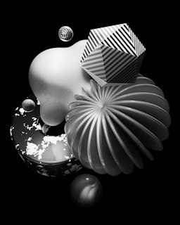 A surreal composition of geometric objects in black, white, and gray tones. The arrangement includes a striped polyhedron, a smooth abstract shape, a spherical object with a uniform stripe pattern, and a textured donut-shaped form. The objects are layered and seem to float against a solid black background, creating a sense of depth and juxtaposition.