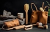 A selection of eco-friendly personal care items including brushes and a pouch, set against a dark background. The arrangement features a variety of wooden brushes with natural bristles and several containers. A fabric pouch and a cloth are also present, adding to the organic feel.