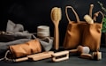 A selection of eco-friendly personal care items including brushes and a pouch, set against a dark background. The arrangement features a variety of wooden brushes with natural bristles and several containers. A fabric pouch and a cloth are also present, adding to the organic feel.
