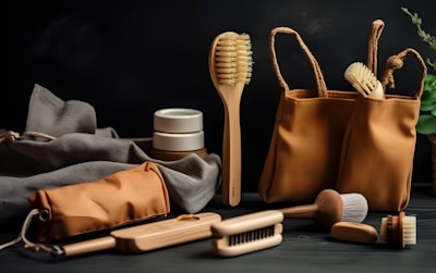 A selection of eco-friendly personal care items including brushes and a pouch, set against a dark background. The arrangement features a variety of wooden brushes with natural bristles and several containers. A fabric pouch and a cloth are also present, adding to the organic feel.