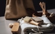 A collection of eco-friendly personal hygiene items is arranged on a soft, white fabric. Included are a wooden brush with natural bristles, a loofah, and other bamboo or wooden accessories, suggesting a focus on sustainability. The scene is softly lit, and a burlap bag is subtly visible in the blurred background.