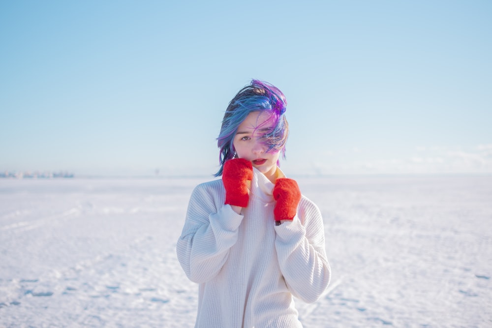 a girl with blue hair and red mittens covers her face