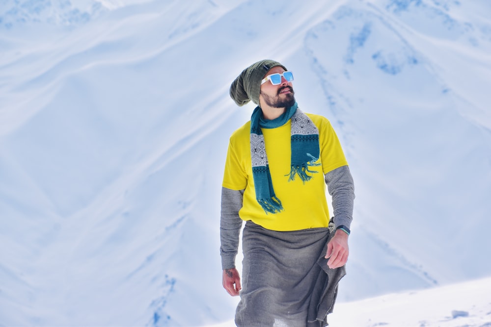 a man wearing a yellow shirt and a hat is standing in the snow
