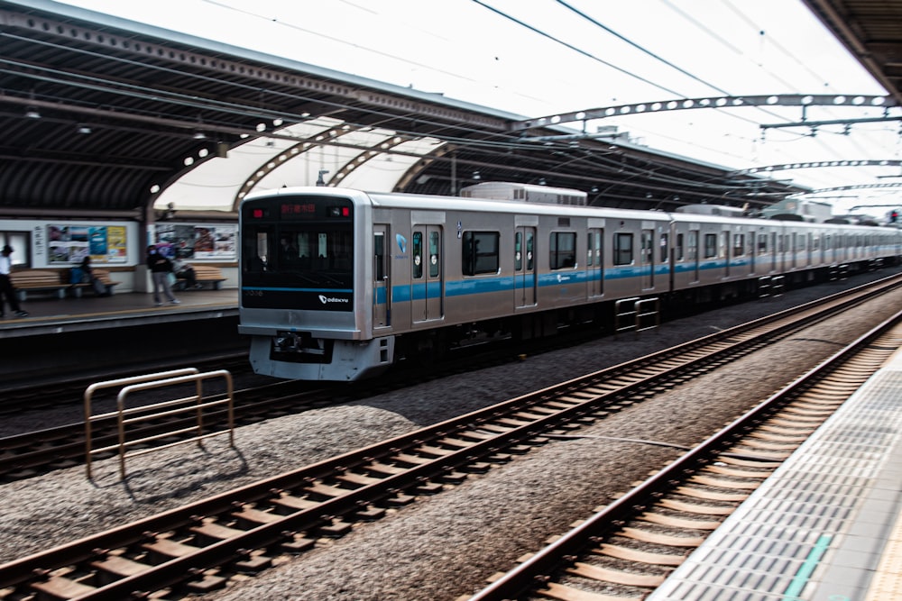 a silver train traveling down train tracks next to a train station