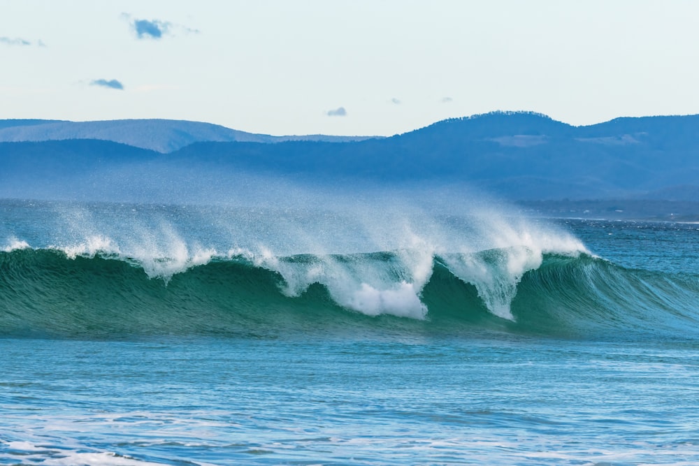 a large wave in the ocean with mountains in the background