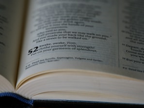 A close-up view of an open book showing text on pages with verse numbers highlighted in bold, focusing on a passage that includes the phrase 'Awake, awake, Zion, clothe yourself with strength'.