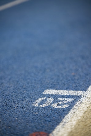 The image contains a close-up view of a running track with a blue surface and a white line marking. The number thirty is visible in white on the track surface near the edge.