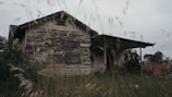 A distressed house needing renovation with overgrown grass.