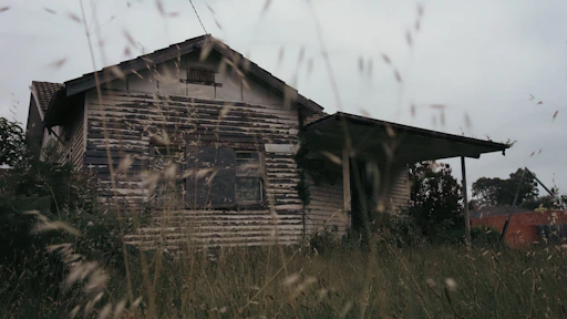 A weathered house with peeling paint and overgrown yard, showing signs of neglect.