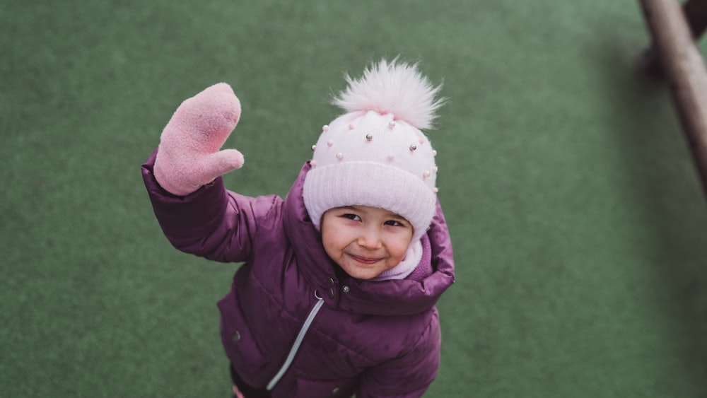 a little girl wearing a purple jacket and a pink hat