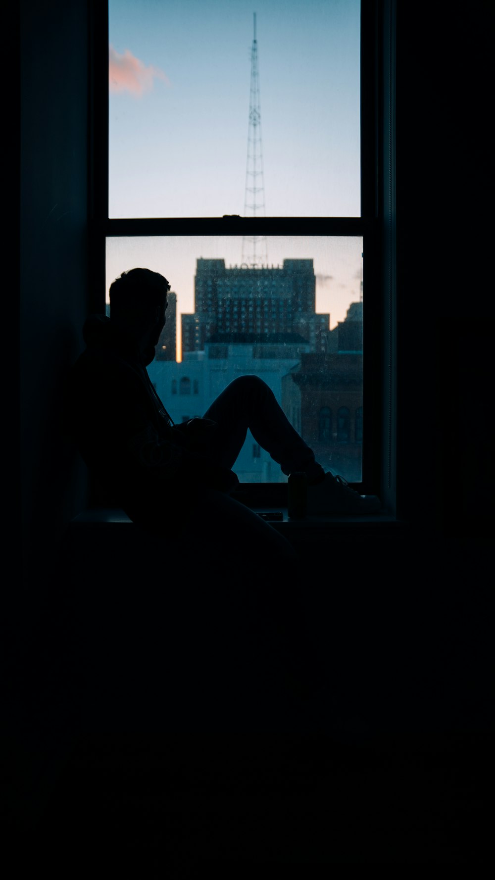 a person sitting in a window sill looking out at the city