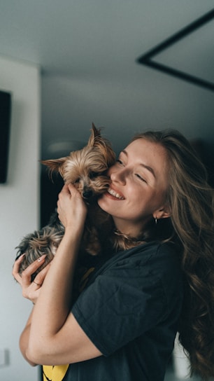 A joyful rescued dog being gently held by a caring volunteer in a sunlit shelter.