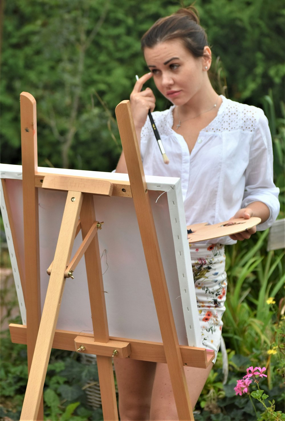 a woman standing next to a easel holding a brush
