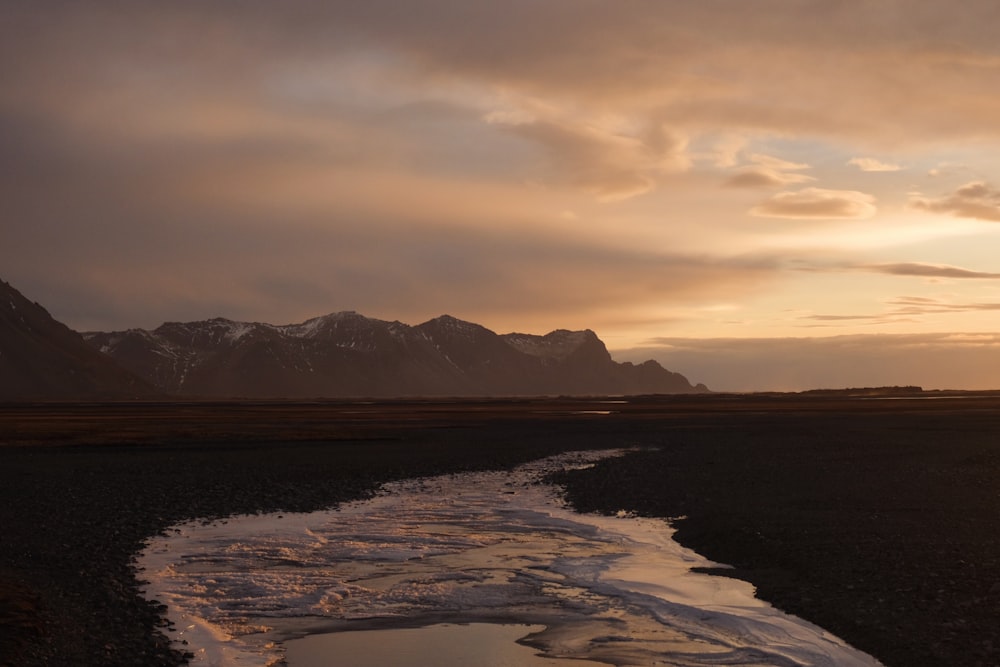 a river running through a field with mountains in the background