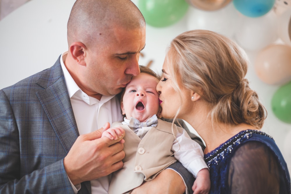 a man and woman holding a baby in front of balloons