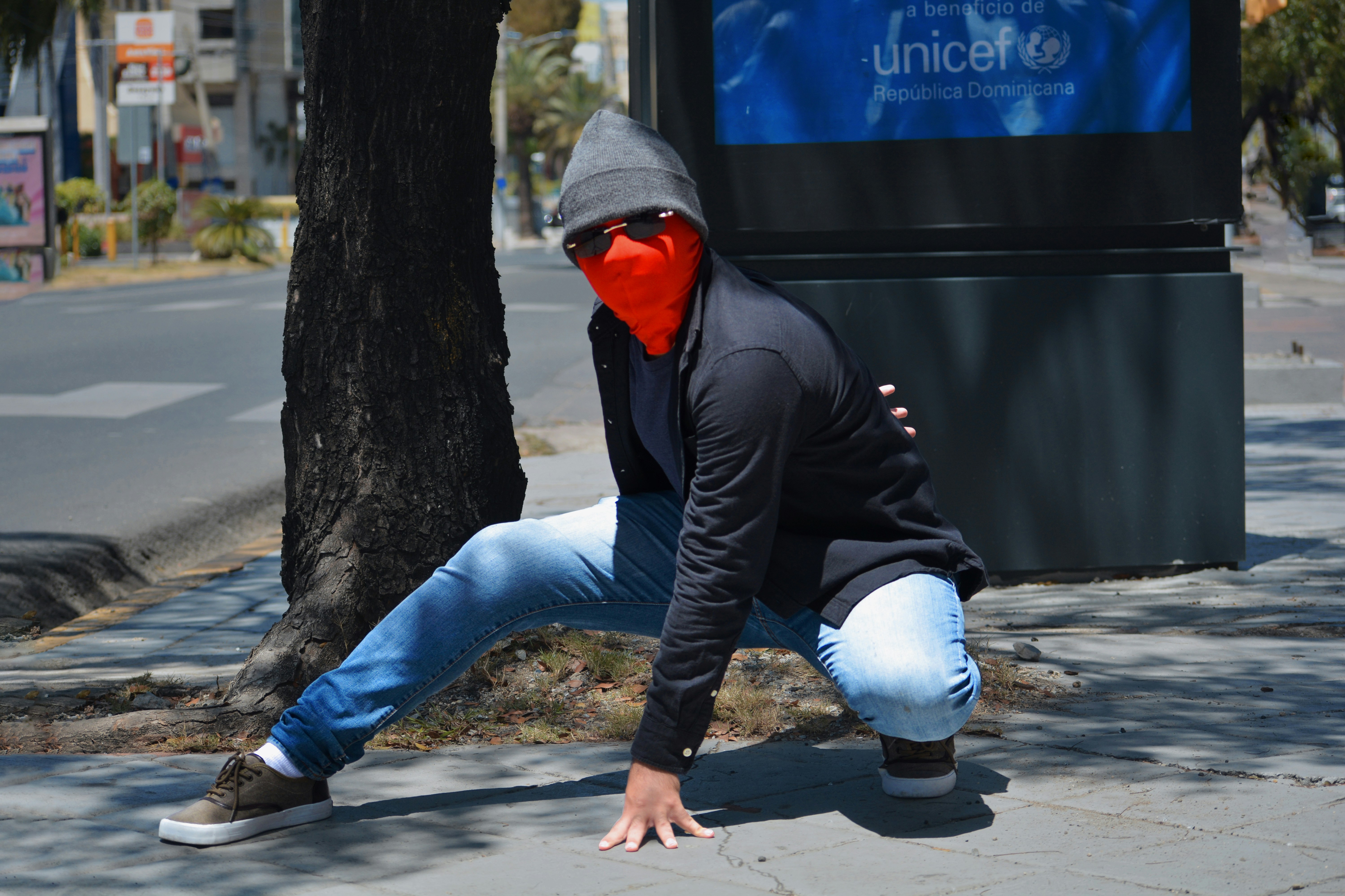 a man in a red mask crouches on a sidewalk