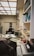 An office space cluttered with various office supplies and equipment. There are several chairs, desks filled with papers, books, and vintage electronics including a CRT monitor, keyboard, and an old typewriter. Shelves filled with binders, books, and file organizers are visible. Lighting is provided by a grid of ceiling panels.