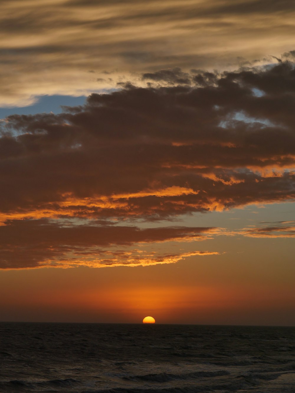 the sun is setting over the ocean on a cloudy day