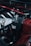 Close-up photo of a car engine featuring a black cylindrical component with a soft cover displaying the words 'CHASE BAYS' in white text. Various metallic engine parts, including hoses and a dipstick, are visible, with predominant colors of red, black, and silver. The setting appears industrial, highlighting the engineered details.