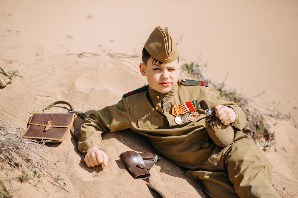 a young boy in a military uniform sitting in the sand
