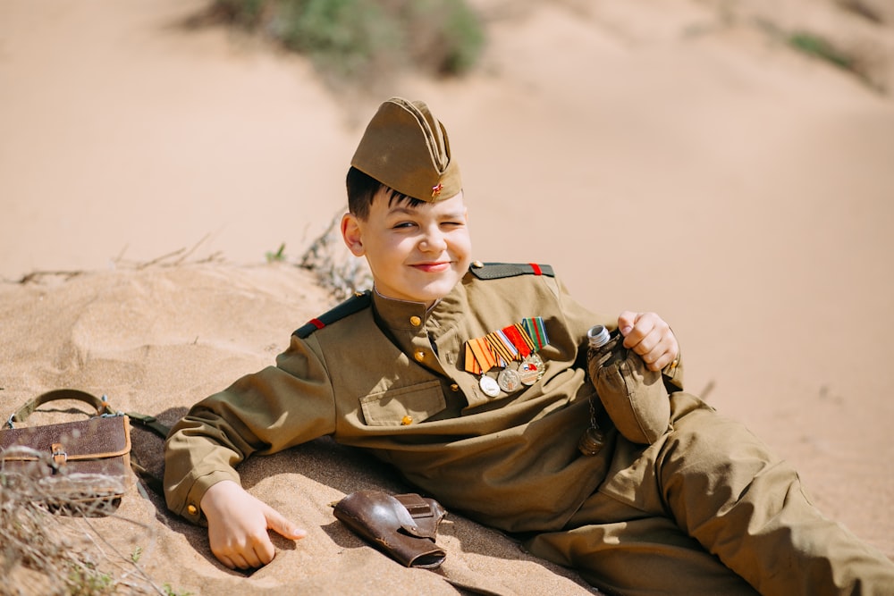 a boy in a military uniform laying on the sand