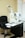 A room equipped with optical diagnostic equipment, including an autorefractor keratometer on a black adjustable table, next to a black swivel chair. The walls and floor are light-colored, and there's a window to the right.