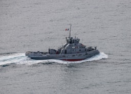 A small military vessel navigates through the ocean, creating a wake in the water. The ship is grey with the identification number A641 visible on its side and a flag flying from its mast.