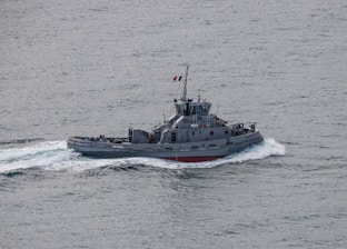 A small military vessel navigates through the ocean, creating a wake in the water. The ship is grey with the identification number A641 visible on its side and a flag flying from its mast.