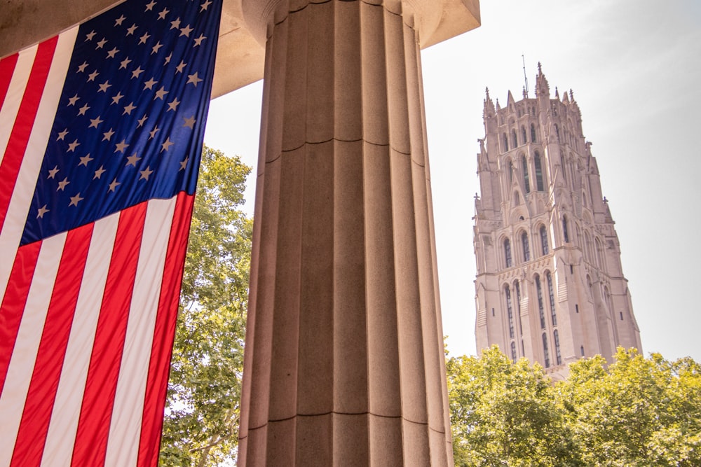 an american flag hanging from a pillar in front of a tall building