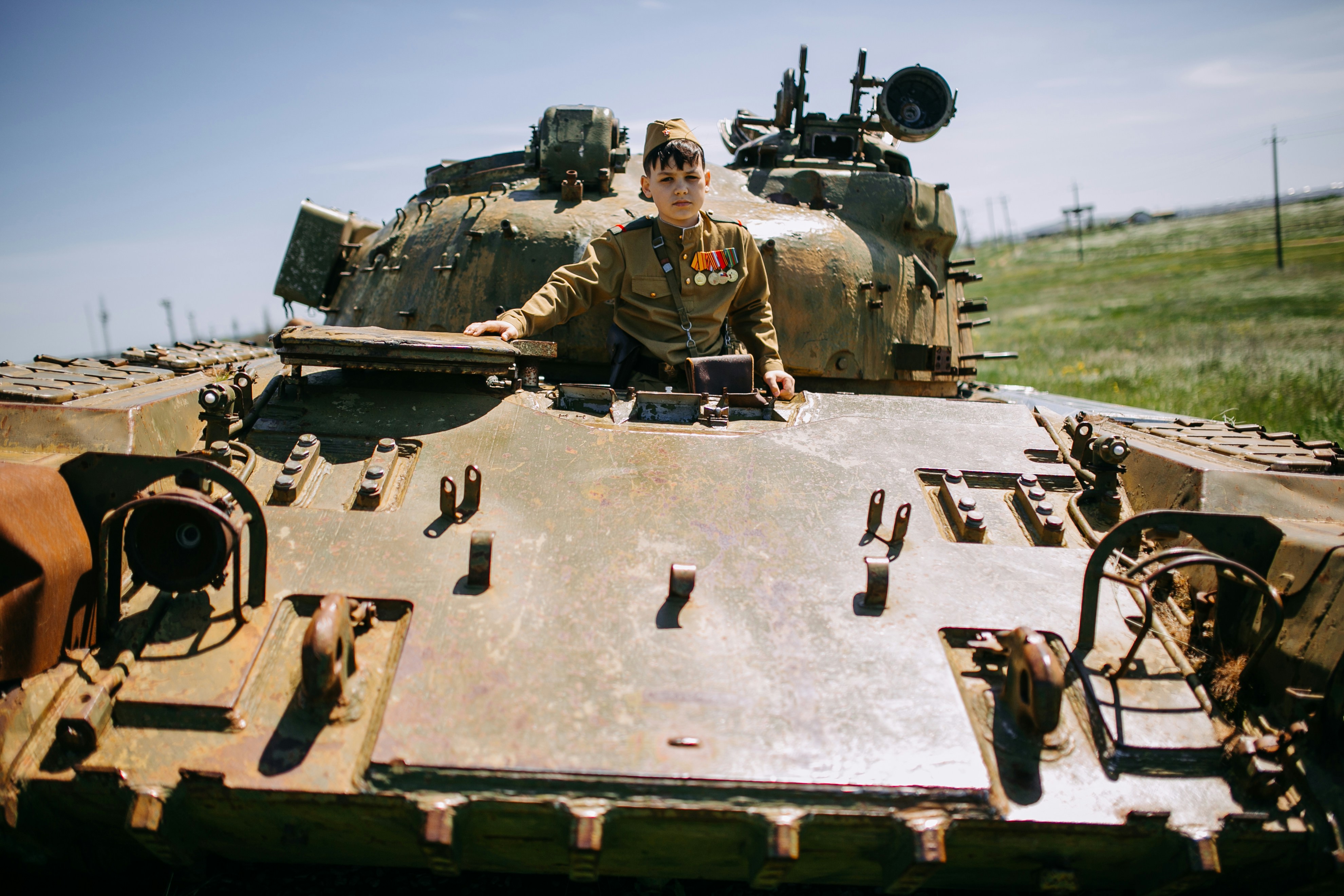 A man sitting on top of a tank in a field photo – Free Boy Image on ...