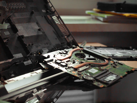 Technician repairing a laptop motherboard with precision tools on a wooden desk.