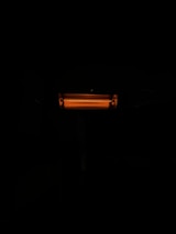 An illuminated electric heater with visible heating coils radiating a warm orange light. The heater is surrounded by darkness, emphasizing the glow of the heating element.