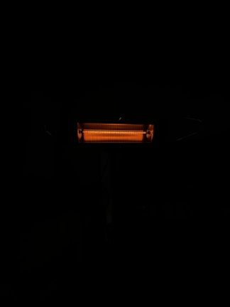 An illuminated electric heater with visible heating coils radiating a warm orange light. The heater is surrounded by darkness, emphasizing the glow of the heating element.