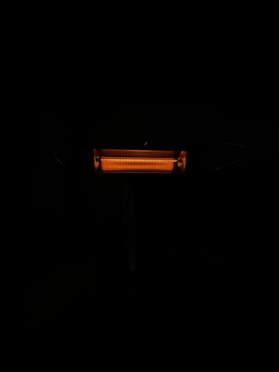 An illuminated electric heater with visible heating coils radiating a warm orange light. The heater is surrounded by darkness, emphasizing the glow of the heating element.