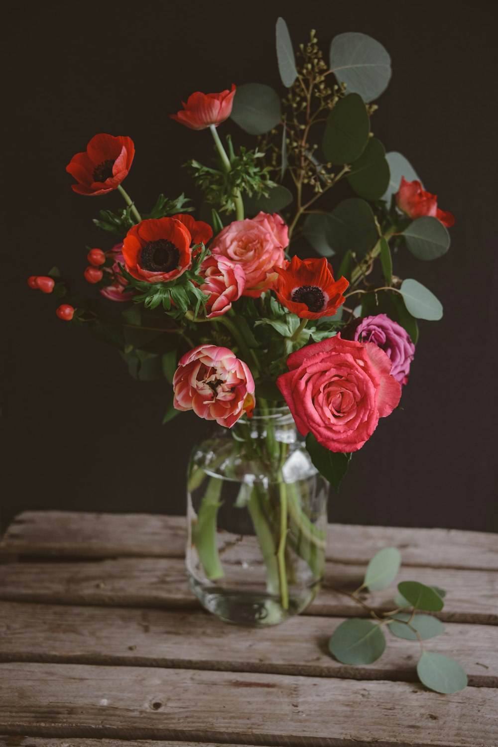 a vase filled with red and pink flowers on top of a wooden table