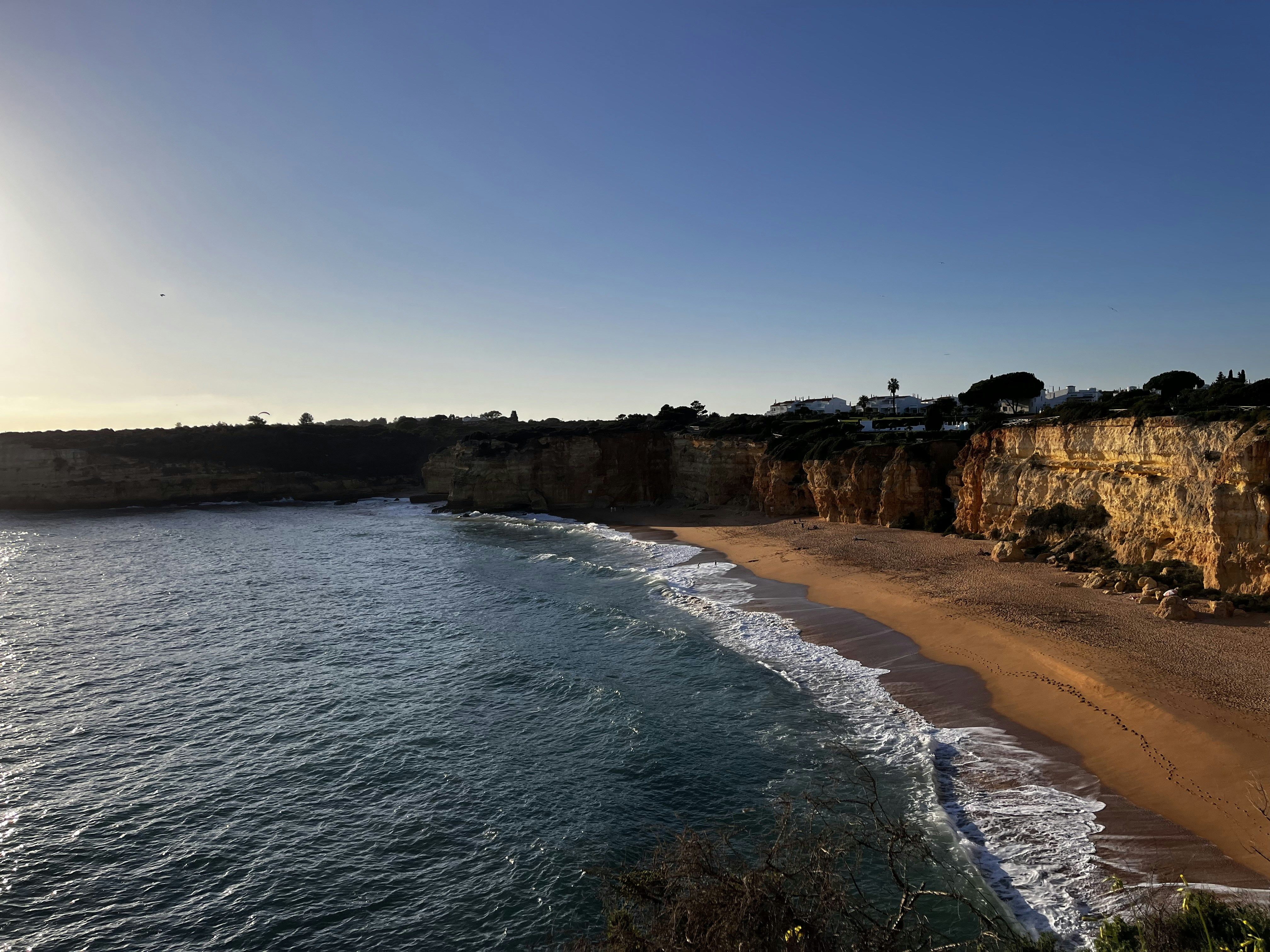 a sandy beach next to a cliff on a sunny day