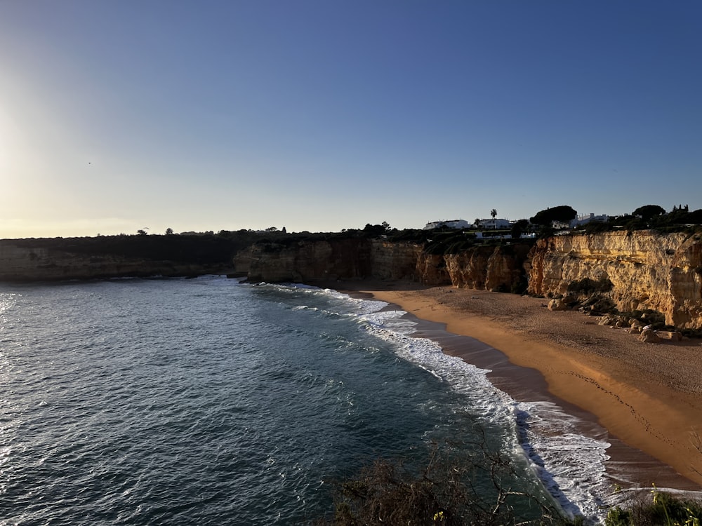 a sandy beach next to a cliff on a sunny day