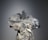 A mannequin is adorned with an elaborate and intricate dress featuring voluminous floral decorations and ribbons. The design includes shimmering elements and textured layers, creating a luxurious and artistic appearance.